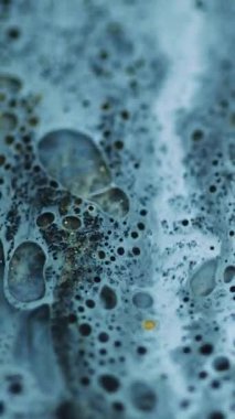 Dikey video. Mürekkep kabarcığı damlıyor. Sanat yağı dökülmüş. Odaklanmamış mavi siyah ıslak köpük emülsiyonu parlak altın parçacıklar dalga hareketleri soyut arkaplan.