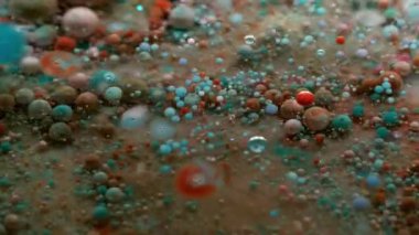 Akışı kes. Pigment dökülmüş. Küçük yuvarlak renk parçacıkları bulanık şeffaf sıvıda yüzen boyaları karıştırıyor. Petrol sanatı suyu soyut arkaplan.