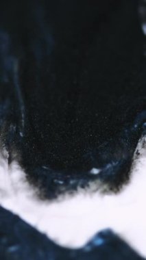 Dikey video. Işıltılı damlama sanatı. Acryl döküldü. Odaklanmamış siyah beyaz lacivert sıvı mürekkep akışı dalga hareketi soyut arkaplan.