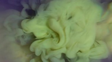 Mürekkep bulutu. Renk sıçraması. Pastel sarı boya damlası mor suda çözünür. Sıvı sanat akışları soyut odaklanmış arka planda dumanlı çekim yapar.