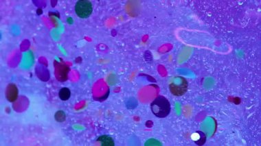 Parlak sıvı. Konfeti döküldü. Dekoratif kıvılcımları olan su mor buz yüzeyinden aşağı akar. Neon mürekkep efektli, odaklanmış renk arkaplanı.