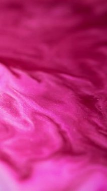 Dikey video. Islak sim dökülmüş. Boya sıçraması. Odaklanmamış morumsu pembe renk parıldayan parçacıklar dokusu sıvı mürekkep harmanı hareket soyut sanat arkaplanı.