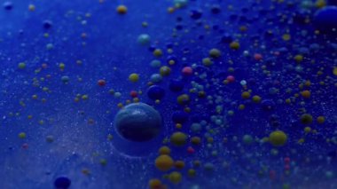 Kabarcık emülsiyonu. Köpüklü sıvı. Mavi parıldayan suda yüzen çok renkli akrilik küreler. Soyut arkaplanda mürekkep damlası karışımı.