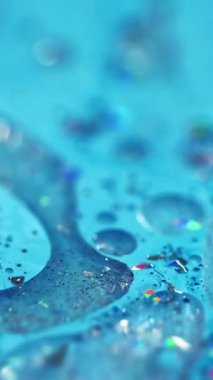 Dikey video. Renk mürekkebi dökülmüş. Parlak yağ kabarcıkları. Odaklanmamış mavi renkli ışıldayan parçacıklar jel damlaları akrilik boya sıvısı parlatıcı doku akış hareketi soyut sanat arka planı.