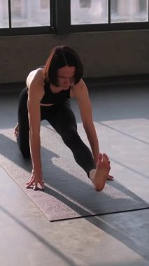 Dikey video. Jimnastik egzersizi. Ayrılma egzersizi. Egzersiz yoga yapan sağlıklı bir kadın güneş ışınları jimnastik salonundaki spor minderinde asana kas esneme egzersizi yapıyor..