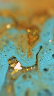 Dikey video. Sıvı sim dökülmüş. Parlak mürekkep. Bulanık mavi altın rengi metalik pullar kabarcıklar sıvı boya karışımı hareket soyut sanat arka planı ve bokeh ışıkları.