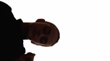 Dikey video. Tasasız siluet. Olumlu neşe. Beyaz fotokopi çekilen arka planda dans etmekten hoşlanan huzurlu ve rahat bir kadının koyu renk kontrastı..