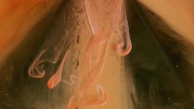 Damlayan mürekkep. Duman akışı. Parlak turuncu şeftali rengi peçe suda yüzüyor. Siyah parlayan piramit üzerinde kayan parlak boya soyut arkaplan bulanıklığı.