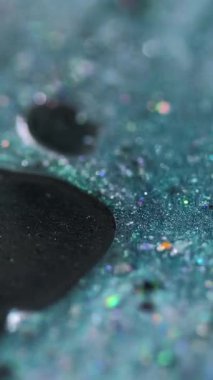 Dikey video. Parlak mürekkep damlası. Boya dökülmüş. Bulanık deniz mavisi siyah holografik pullu parçacıklar yağ jeli sıvı emülsiyon soyut sanat arka planı ve bokeh ışıkları.