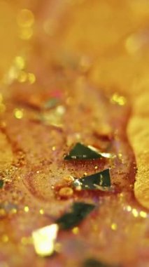 Dikey video. Köpüklü yağ damlası. Parıltılı boya döküldü. Bulanık altın rengi parlak metalik pullu parçacıklar mürekkep parlatıcısı sıvı hareket soyut sanat arkaplanı ve bokeh ışıkları.