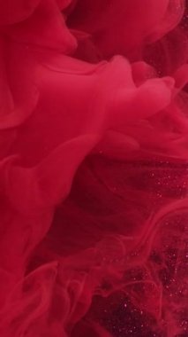 Dikey video. Parıltılı resim. Sigara içme sanatı. Suyun altında dönen renkli sis pigmenti. Soyut mor mürekkep arka planında parlak kırmızı turuncu.