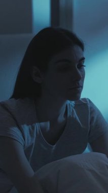 Dikey video. Gece endişesi. Uykusuzluk hastalığı. Yorgun, yalnız, depresif, uykulu, aşırı düşünen, iç çeken, karanlık yatak odasında geç saatlere kadar esneyen bir kadın..