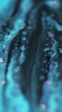 Dikey video. Parlak bir dökülme. Akrilik boya. Odaklanmamış mavi renkli holografik simli parçacıklar yüzen baloncuklar boya sıvı karışımı akış hareketi soyut sanat arka planı.