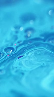 Dikey video. Akrilik boya akışı. Parlak sıvı damlası. Odaklanmamış mavi renkli ışıldayan parçacıklar kabarcıklar su boyası sıvı mürekkep harmanlama hareketi soyut sanat arkaplanı.