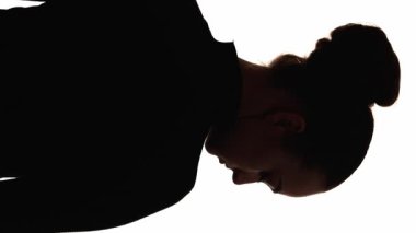 Dikey video. Sinirli siluet. Yalnızlık melankolisi. Koyu kontrastlı arka plan çizgisi, üzgün depresif kadının başını beyaza çevirmesi..