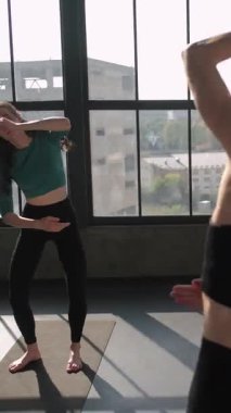 Dikey video. Yoga dersi. Esneme antrenmanı. Spor dersi. Spor salonundaki fitness minderi spor salonunda aktif giyimli insanlarla jimnastik denge egzersizi yapan bayan eğitmen..