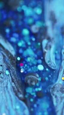 Dikey video. Parlak sıvı dökülmüş. Parlak mürekkep dokusu. Bulanık mavi, parlak pullu pullu parçacıklar akrilik boya, sıvı damlalar, soyut sanat arka planı, bokeh ışıkları..