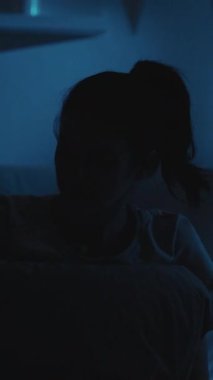 Dikey video. Taşınabilir endişe. Gece hüsranı. Kızgın kadın, karanlık yatak odasında telefonunu fırlatıp yastığını yumrukluyor..