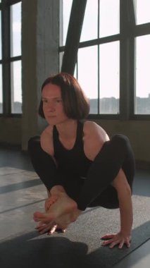 Dikey video. Yoga pratiği. Denge çalışması. Spor elbiseli bir kadın spor salonunda spor salonunda spor salonunda jimnastik egzersizi yaparken amuda kalkma kurbağası pozu veriyor..
