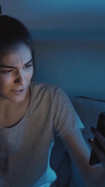 Dikey video. Gece sohbeti. Sanal arama. Uzaktan iletişim. Heyecanlı uykusuz kız gecenin geç saatlerinde karanlık yatak odasında telefonda konuşuyor..