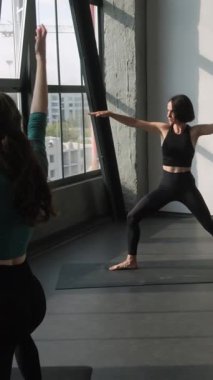 Dikey video. Yoga eğitmeni. Spor salonu. Atletik bayan spor antrenörü aktivite kıyafetleri grubunda insanlar denge egzersizi yapıyor. Asana pozu, kapalı spor salonunda vücut duruşu, kapalı spor salonunda..