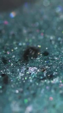 Dikey video. Sıvı pırıltılı boya. Islak sim damlası. Bulanık deniz mavisi siyah holografik pullu parçacıklar parlak jel sıvısı mürekkep sızıntısı soyut sanat arka planı ve bokeh ışıkları.