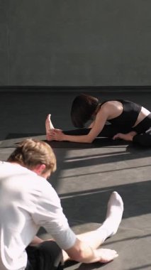 Dikey video. Jimnastik dersi. Yoga egzersizi. Spor eğitmeni kadın spor eğitmeni. Spor salonundaki spor salonundaki paspasın üzerinde vücut esnetme egzersizi yapan insanlar..