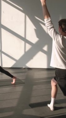 Dikey video. Yoga dersi. Grup çalışması. Aktif insanlar, spor salonundaki spor salonundaki spor paspası üzerine kadın spor eğitmeniyle esneme egzersizi yapıyor..