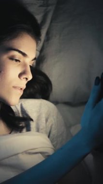 Dikey video. Gece online. Uyku zamanı aleti. Mobil uykusuzluk. Uykucu kız, internetten telefon kullanıyor internette geziniyor, geç saatlere kadar yatakta esniyor..