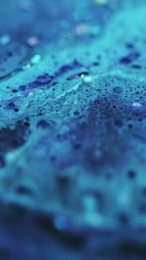 Dikey video. Parıldayan sıvı dökülmüş. Renk köpüğü dokusu. Odaklanmamış mavi ışıldayan pullu partiküller yağ kabarcıkları akrilik boya mürekkebi emülsiyon sıvı akış hareketi soyut sanat arka planı.