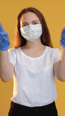 Dikey video. Merhameti destekleyin. Aşk bakımı. COVID-19 salgını. Korunaklı maske eldivenli kadın sarı renkte kalp şekli çiziyor..