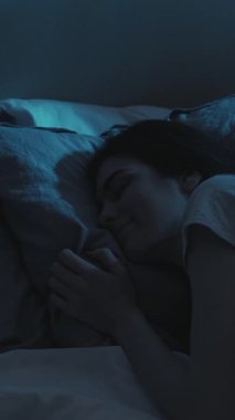 Dikey video. Gece uykusu. Huzurlu bir uyku. Rahatlamış, mutlu bir kadın, karanlık yatak odasında yumuşak, yumuşak bir yastığın üzerinde rüya görüyor..
