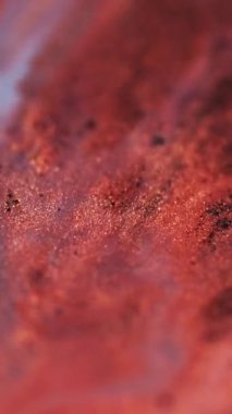 Dikey video. Jel gölgeleri. Parıltılı boya akışı. Parlak sıvı. Bokeh ışığı. Odaklanmamış kırmızı renkte parıldayan pullu parçacıklar su emülsiyonunda titreşiyor soyut sanat arka planında yayılıyor.