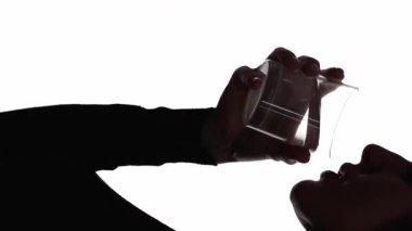 Dikey video. Su dengesi. Sıvı diyeti. Tazeleme detoksu. Koyu kontrast profili silueti, beyaz bardaktan saf mineral içen susamış bir kadın silueti..