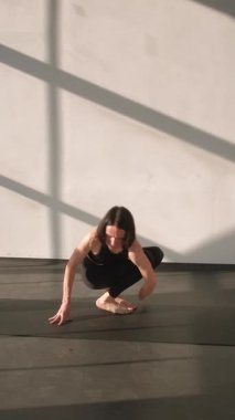 Dikey video. Esneme esnekliği. Denge yogası. Spor salonundaki spor elbiseli kadın amuda kalkma egzersizi asana, spor salonundaki spor paspası üzerine jimnastik yapıyor..