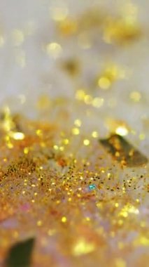 Dikey video. Işıldayan sıvı. Islak sim dokusu. Odaklanmamış altın rengi parlak metalik pullu partiküller akışkan akış hareketini soyut sanat arkaplanını bokeh ışıkları ile parlatıyor.