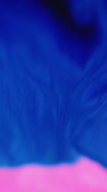 Dikey video. Renkli jel damlası. Boya karışımı. Odaklanmamış pembe pigment şeffaf simli parçacıklar yağ emülsiyon damla karışımı sanat soyut arkaplan yayıyor.