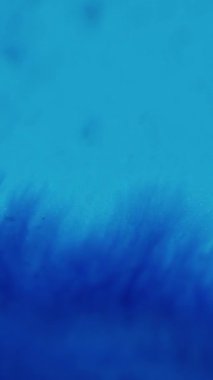 Dikey video. Parlayan sıvı. Yapışkan damlalar. Parlak mürekkep dokusu. Odaklanmamış parlak mavi renk parıldayan boya karışımı dalga hareketinin soyut sanat arkaplanı.