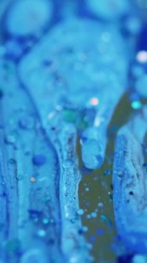 Dikey video. Akrilik sıvı damlası. Parıltılı boya döküldü. Odaklanmamış mavi renkli parlak pullu partiküller parlaklığı desen su emülsiyon sıvı mürekkep akışı hareket soyut sanat arka planı.