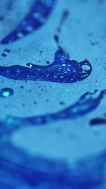 Dikey video. Mürekkep akışı. Banyo köpüğü dokusu. Odaklanmamış mavi renkli parlak partiküller yağlı baloncuk sıvısı emülsiyon sıvı damlama hareket soyut sanat arka planı.