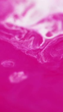 Dikey video. Akrilik sıvı dökülmesi. Sıvı mermer dokusu. Bulanık beyaz pembe renkli girdap katmanları mürekkep damlaları parlak parıltılı yüzeyli soyut sanat eserlerine dökülüyor..