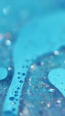 Dikey video. Parıltılı bir karışım. Akrilik boya dökülmüş. Bulanık mavi renk parlak pullu parçacıklar jel sıvısı yüzen kabarcıklar mürekkep emülsiyon sıvı akım hareket soyut sanat arka planı.