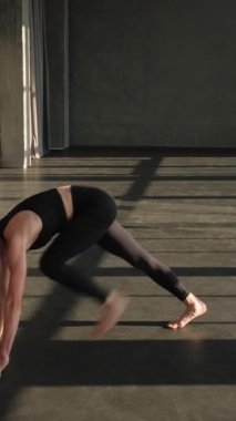 Dikey video. Jimnastik pozisyonu. Esneme egzersizi. Aktif giyinen sağlıklı bir kadın yoga esnekliği egzersizi yapıyor. Boş spor salonu stüdyosunun içinde tek başına egzersiz yapıyor..
