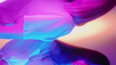 Dikey video. Ultraviyole kız. Neon pozu. İki kadın model, parlak renkli LED tüpleriyle kameranın önünde hareket ediyor. Disko dumanı stüdyo konsepti.