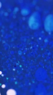 Dikey video. Sıvı sim damlası. Yağ sıvısı. Odaklanmamış mavi renk parçacıkları parıldayan boya damlaları pigment su mürekkebi emülsiyon hareket soyut sanat arka planı.