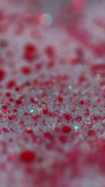 Dikey video. Mürekkep damlası. Parlak sıvı dokusu. Bulanık, kırmızı, parlak, pullu, şeffaf, sıvı, boya damlaları. Bokeh ışıklarıyla hareketli, soyut sanat arkaplanı..