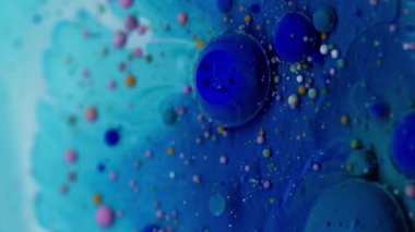 Dikey video. Baloncuk döküldü. Mürekkep akışı. Yağ renkli damlalar mavi sıvıda eriyor. Su soyut sanat arka planında yüzen akrilik pigmentler.