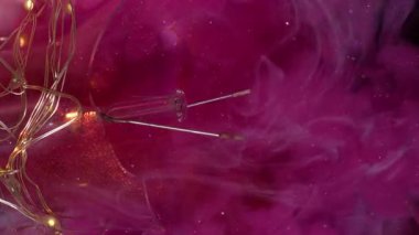 Dikey video. Duman sıçrıyor. Sis dalgası. Pembe akarsu boyası, siyah arka planda beyaz peçeyi karıştırıyor. Değişen parıldayan sanatsal sıvı cam kırıkları ampulü yakar.