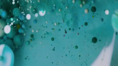 Dikey video. Köpüklü sis. Pigment dökülmüş. Yuvarlak turkuaz mavi parçacıklar bulanık şeffaf sıvıda boya dökülmesini karıştırıyor. Petrol sanatı suyu soyut arkaplan.