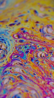 Dikey video. Boya damlacıkları. Yağlı gökkuşağı. Odaklanmamış mor yeşil sıvı boya eğrisi koyu siyah bulanık ışık soyut sanat arka planında akrilik kaygan.